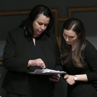 Två kvinnor klädda i svart ser på ett papper som den ena kvinnan har i handen.