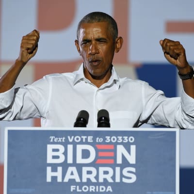 Barack Obama talar stående bakom ett podium klädd i vit skjorta med ärmarna uppkavlade.