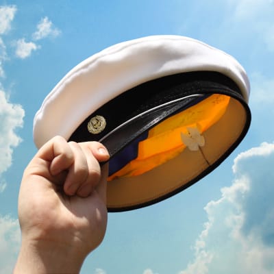 En hand som håller upp en studentmössa mot en blå himmel