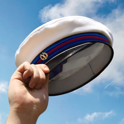 En hand som håller i en examensmössa mot en blå himmel