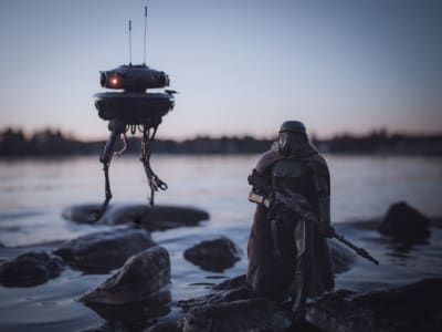 En leksaksfigur föreställande en soldat från Star wars. Den står på en sten vid en strandkant. I bakgrunden syns också en robot från Star wars. 