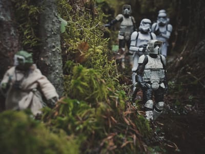 Leksaksfigurer föreställande soldater från Star wars. De går i en skog och i förgrunden syns en annan figut som gömmer sig. 