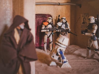 Leksaksfigurer föreställande soldater från Star wars, samt en robot och Obi Wan Kenobi. Soldaterna vaktar en dörr och Obi Wan gömmer sig i förgrunden. 