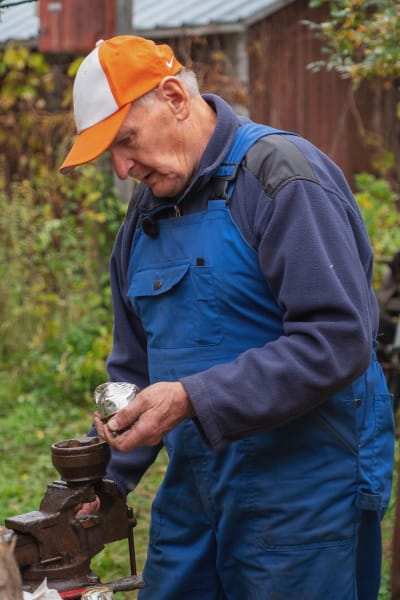 Lippalakkipäinen mies tekee vanhasta juomatölkistä silmää Villasarvikuono-veistokselle.