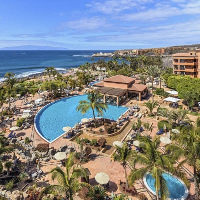 Ett hotell med terracottabruna väggar, en pool och palmer.