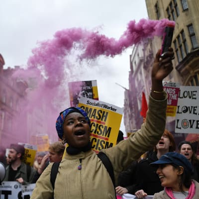 Joukko mielenosoittajia. Naisella kädessään vaaleanpunaista savua levittävä pakkaus.