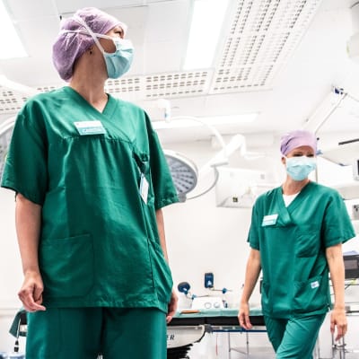 Två sjukskötare klädda i grönt och med munskydd arbetar i operationssal.