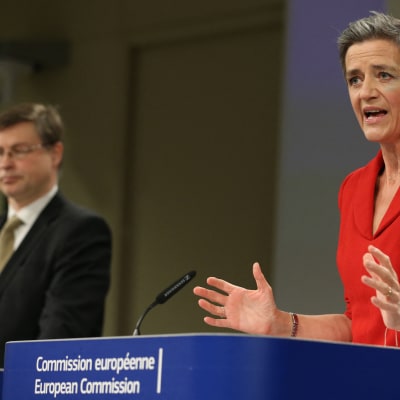 Margrethe Vestager tiedotustilaisuudessa, taustalla näkyy Dombrovskis.