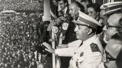Spaniens framlidna diktator Francisco Franco står omgiven av personer på en balkong, i bildens vänstermiljö syns en stor folkmassa. 
