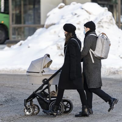 Ett par går med barnvagn på en snöig gata i Hagnäs i Helsingfors.
