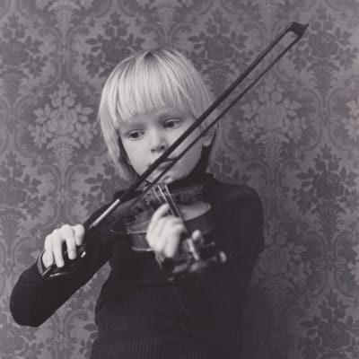 Anssi Kela soittaa viulua seitsemänvuotiaana vuonna 1979 Kauniaisissa. Mustavalkoinen kuva, Anssilla tumma villapaita päällä.