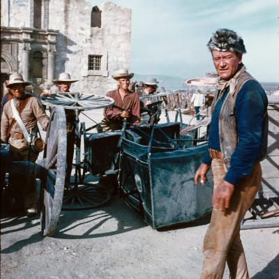 Mies (John Wayne) seisoo tiesulun ja taakse asettautuneiden muutaman miehen edessä.