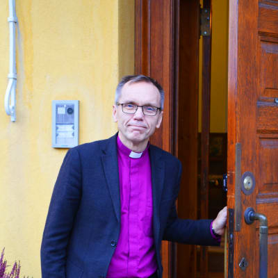 En man står utomhus och håller upp en ytterdörr.