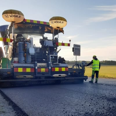 Asfaltointikone päällystää maantietä, koneen edustalla seisoo työntekijä.