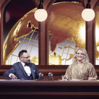 Riku Rantala ja Jenni Poikelus istuvat Hengaillaan lavasteessa pöydän takana.