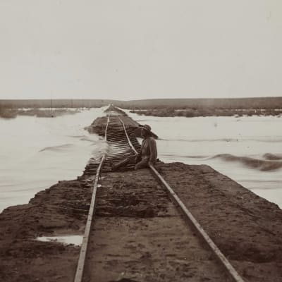 En man sitter på en översvämmad järnväg mellan Keetmanshoop och Lüderitz i dåvarande Tyska Sydvästafrika, nuvarande södra Namibia. Bilden är tagen omkring 1910.