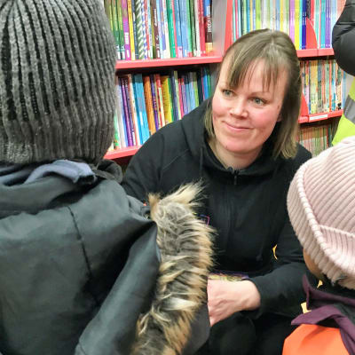 Specialbibliotekarie Michelle Mattfolk talar med några barn, som syns med ryggen mot kameran. I bakgrunden bokhyllor med böcker.