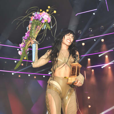 Loreen håller i ett pris och blommor medan hon ler på scenen.
