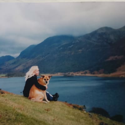 Elisa Aaltola istuu koiran kanssa skotlantilaisessa järvi- ja vuoristomaisemassa.