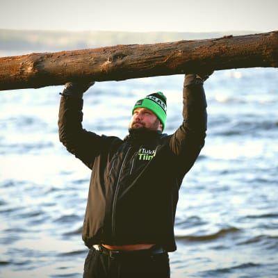 Mika Törrö lyfter en stock över huvudet på stranden
