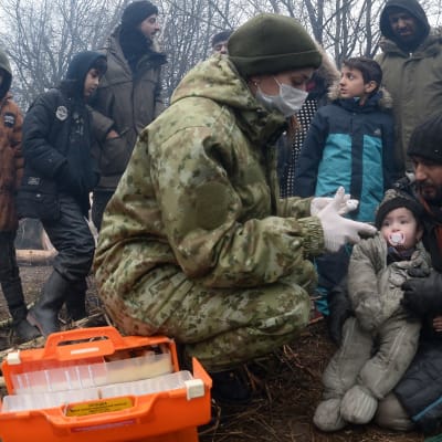 En läkare utför hälsokoll på en pappa och hans barn i ett migrantläger. 