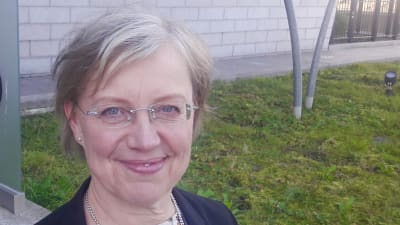 Maija Sakslin står vid en invaskylt.