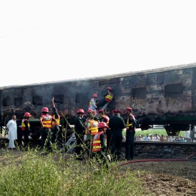 Räddningsarbetare utanför de brandskadade tågvagnarna i Pakistan.