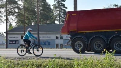En cyklist cyklar på en riksväg. Framför cyklisten kör en lastbil.