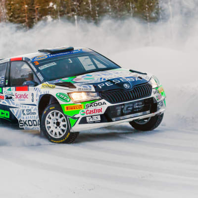 En rallybil susar fram på en snötäckt väg.