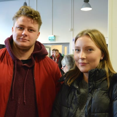 en kille och en tjej med ytterkläderna på inomhus bland andra människor