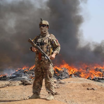 En soldat från Afghanistans regeringsstyrkor står vid ett markområde där det brinner.