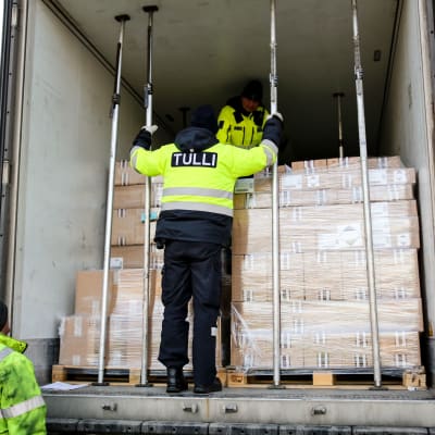 Tulltjänstemän granskar en last med bruna lådor i en lastbil. 