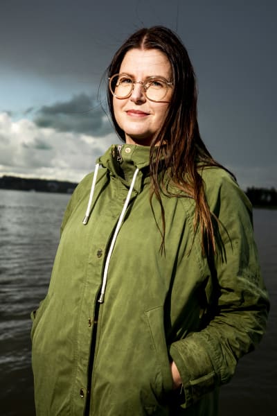 En kvinna med grön jacka och glasögon på en brygga.
