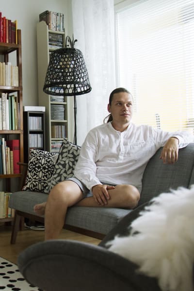Kasper sitter i en soffa som står framför en stor bokhylla. 