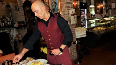Man med rött förkläde serverar tryffelpasta på restaurang i staden Fabriano.