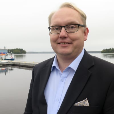 Kari Tolonen seisoo järven rannassa. Taustalla näkyy laituri ja veneitä.