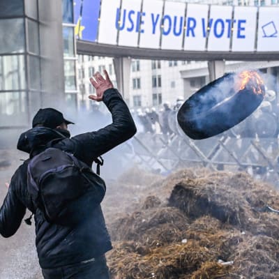 Demonstrerande bönder kastar brinnande bildäck framför polisen i Bryssel under ett EU-toppmöte.