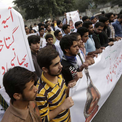 Miehiä mielenosoituksessa, julisteessa kuva Asia Bibistä hirttoköydessä.