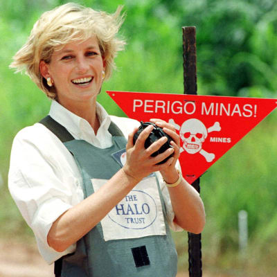 En leende kvinna håller i en granat framför en skylt som varnar för minor.