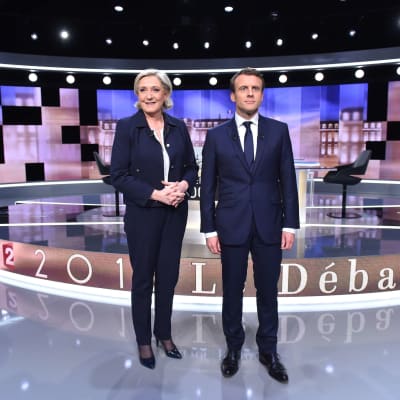 Marine Le Pen ja Emmanuel Macron seisovat keskellä suurta televisiostudiota. Taustalla näyttöruutuja ja pöytä, jonka ympärillä väittely pidettiin.