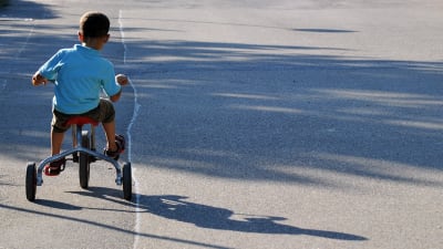 En pojke cyklar med stödhjul på en tom väg.