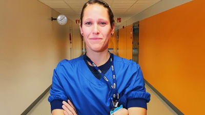En intensivvårare tittar rakt in i kameran i en sjukhuskorridor. Kvinnan har armarna i kors.