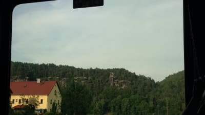 bild tagen från ett tågfönster, på bilden syns skog och berg och ett stort gult egnahemshus med rött tak.
