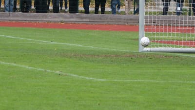 Fotboll går in i mål vid stolproten.