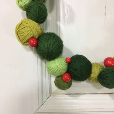 Krans gjord av gröna garnnystan, dekorerad med röda träkulor