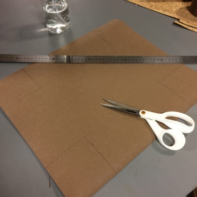 Pappersläder med markerade hörn och sax och linjal på ett bord.