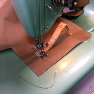 Symaskin med nålen nere i korktyg som sys fast på pappersläder.