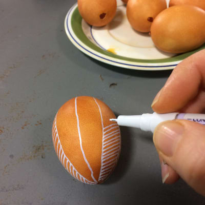 Brunt ägg på vilket det ritas ränder med vit tusch.