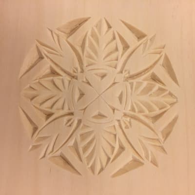En ljus träskiva som dekorerats med ett runt ornament i träsnitt.