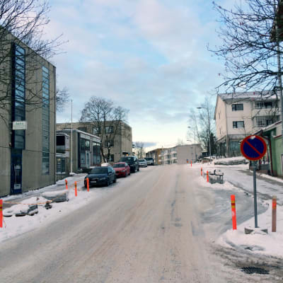 En snöbeklädd väg. Till vänster syns parkerade bilar.